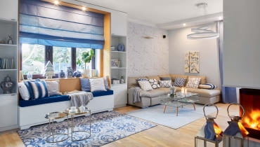 W salonie zwracają uwagę dodatki - chińskie wazy, poduchy w paski i marokańską koniczynkę, wzorzysty dywan (z Mint Grey i Raw Decor). Do tapety z motywem kwitnących gałązek wiśni idealnie pasuje obraz Ivy Białopiotrowicz, na którym rozsiadło się żółte ptasie stadko. Kominek, poprzednio zainstalowany pośrodku salonu, został zamieniony na model narożny, tak by był widoczny zarówno z salonu, jak i jadalni. Światło i wzór: spójrzmy czasem w górę. Ciekawa lampa sufitowa potrafi naprawdę przykuć wzrok. Dla całej rodziny bardzo ważne jest wspólne spędzanie czasu. Stąd pomysł na dodatkowe wygodne siedzisko w salonie. Umieszczono je we wnęce - do jej zbudowania wystarczyły dwie wysokie szafki po bokach okna i rama z płyty gipsowo-kartonowej. Zainstalowano w niej oświetlenie. Złote stoliki kawowe są z Zara Home. W salonie zwracają uwagę dodatki - chińskie wazy, poduchy w paski i marokańską koniczynkę, wzorzysty dywan (z Mint Grey i Raw Decor). Do tapety z motywem kwitnących gałązek wiśni idealnie pasuje obraz Ivy Białopiotrowicz, na którym rozsiadło się żółte ptasie stadko. Kominek, poprzednio zainstalowany pośrodku salonu, został zamieniony na model narożny, tak by był widoczny zarówno z salonu, jak i jadalni. Światło i wzór: spójrzmy czasem w górę. Ciekawa lampa sufitowa potrafi naprawdę przykuć wzrok. Dla całej rodziny bardzo ważne jest wspólne spędzanie czasu. Stąd pomysł na dodatkowe wygodne siedzisko w salonie. Umieszczono je we wnęce - do jej zbudowania wystarczyły dwie wysokie szafki po bokach okna i rama z płyty gipsowo-kartonowej. Zainstalowano w niej oświetlenie. Złote stoliki kawowe są z Zara Home.