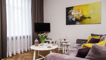 Po przeciwnej stronie kącika jadalnego zaaranżowano salon - na zasadzie przeciwwagi urządzono go w nowoczesnym klimacie. Rozkładana sofa i poręczne stoliki kawowe tworzą wygodną strefę wypoczynku. Tu również znalazło się miejsce dla sztuki - na ścianie pejzaż Rogera Lane. aranżacje wnętrz, zdjęcia mieszkań, mieszkanie w Krakowie