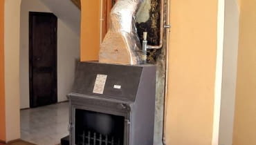 Widoczne naczynie wyrównawcze z zaworem pływakowym zamontowane nad korpusem kominka