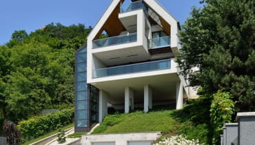 Dom jest wsparty na czterech smukłych, blisko dziesięciometrowych kolumnach i częściowo naturalnej półce w skarpie wzgórza dom jednorodzinny