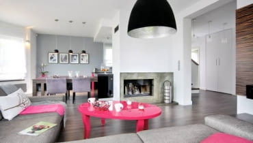 Wystrój domu miał być stonowany kolorystycznie, z przewagą naturalnych barw ziemi. I taki jest. wystarczyło kilka akcentów w ostrym różu, by wnętrza nie wyglądały monotonnie. <BR /> DOM. Ściana z kominkiem oddziela część kuchenno-jadalną od wypoczynkowej. We wnętrzu przeważa kolor szary. Takie są zarówno ściany (także ta z przecierkami, będąca obudową kominka), jak i zrobiona na zamówienie duża kanapa oraz krzesła przy kuchennym stole.