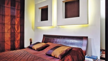 Łóżko stoi na ogół przy najbardziej widocznej ścianie w sypialni. Żal byłoby jej nie wykorzystać - do celów praktycznych albo dekoracyjnych, a najlepiej do obu jednocześnie. Zobaczcie, jak z głową zaaranżować miejsce za głową. <BR > Aranżacje wnętrz. W ramach ozdoby. Oryginalną dekoracją ściany są tu dwie grube ramy z płyty gipsowo-kartonowej. Ich środki wykończono tynkiem strukturalnym pomalowanym farbą w takim samym odcieniu jak meble i dodatki. Te nietypowe konstrukcje posłużyły również do ukrycia oświetlenia zastępującego gospodarzom lampki nocne.