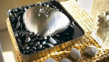 Fontanna domowa. Woda wypływa z czubka stalowej bryły wprost na okalające ją kamyki. Projekt marki Blomus, wys. 8 cm, szer. 32 x 28 cm. Cena: ok. 950 zł, www.fabrykaform.pl Fontanna domowa.