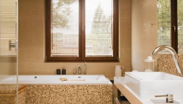 <B> Pojedynczy nie zdziała we wnętrzu wiele, ale w grupie zyskuje moc - ożywia kolorystykę, podkreśla kształt mebli i urządzeń, zdobi. W łazienkach nastał czas mozaiki. </B><BR /> WNĘTRZA: Gospodarze wykończyli mozaiką obudowę wanny oraz ścianę przy umywalce i w kabinie prysznicowej, a więc miejsca najbardziej narażone na kontakt z wodą (wybrano produkt z polerowanego marmuru Emperador włoskiej firmy Sicis). W ten sposób wizualnie podkreślono też strefy mycia i kąpieli. Oprócz mozaiki w łazience zastosowano gres imitujący polerowany trawertyn (płytki 30 x 90 cm i 60 x 90 cm układane na przemian). Odcienie kamienia idealnie pasują do kolorystyki całego wnętrza - na kostkach powtarzają się barwy pozostałych elementów wyposażenia (biel ceramiki, brąz mebli i dodatków, beż gresu). Ciepłe odcienie budują klimat sprzyjający odpoczynkowi. Lustro nad umywalką od góry i od dołu otaczają pasy mozaiki tworzące rodzaj ramy. Do wanny dobudowano schodek wykończony (tak jak cała podłoga) płytami gresu imitującego polerowany trawertyn. W podwieszonym suficie zainstalowano halogeny - dzięki temu można było zrezygnować ze światła sufitowego o dużej mocy i zawiesić jedynie ozdobną lampkę. <B> Pojedynczy nie zdziała we wnętrzu wiele, ale w grupie zyskuje moc - ożywia kolorystykę, podkreśla kształt mebli i urządzeń, zdobi. W łazienkach nastał czas mozaiki. </B><BR /> WNĘTRZA: Gospodarze wykończyli mozaiką obudowę wanny oraz ścianę przy umywalce i w kabinie prysznicowej, a więc miejsca najbardziej narażone na kontakt z wodą (wybrano produkt z polerowanego marmuru Emperador włoskiej firmy Sicis). W ten sposób wizualnie podkreślono też strefy mycia i kąpieli. Oprócz mozaiki w łazience zastosowano gres imitujący polerowany trawertyn (płytki 30 x 90 cm i 60 x 90 cm układane na przemian). Odcienie kamienia idealnie pasują do kolorystyki całego wnętrza - na kostkach powtarzają się barwy pozostałych elementów wyposażenia (biel ceramiki, brąz mebli i dodatków, beż gresu). Ciepłe odcienie budują klimat sprzyjający odpoczynkowi. Lustro nad umywalką od góry i od dołu otaczają pasy mozaiki tworzące rodzaj ramy. Do wanny dobudowano schodek wykończony (tak jak cała podłoga) płytami gresu imitującego polerowany trawertyn. W podwieszonym suficie zainstalowano halogeny - dzięki temu można było zrezygnować ze światła sufitowego o dużej mocy i zawiesić jedynie ozdobną lampkę.