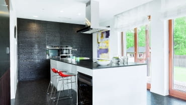 W tym domu rodzina i znajomi najchętniej zbierają się wokół dwóch mebli - stołu w jadalni oraz wyspy, zajmującej w kuchni centralne miejsce. Jest ona na tyle duża (323 x 123 cm), że może przy niej wspólnie gotować kilka osób, nie przeszkadzając sobie nawzajem; mniej zaangażowani w pracę będą w tym czasie"kibicować", siedząc na stołkach barowych. Całą kuchnię zaaranżowano w czerni i bieli; blat wyspy i podłoga są z granitu, fronty wysokiej zabudowy - z płyty MDF fornirowanej szczotkowanym i bejcowanym dębem.