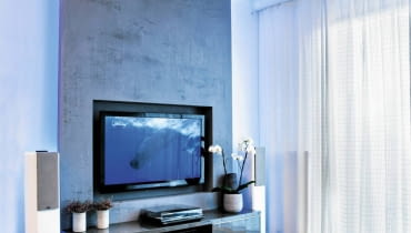 <B> Dawniej potrzebowały solidnej szafki, dziś lekkie i płaskie telewizory coraz częściej wieszamy na ścianie. Projektanci wnętrz proponują różne rozwiązania, dzięki którym miejsce do oglądania wygląda ładnie i jest wygodne. </B><BR /> TELEWIZORY: Projektant chciał, aby salon wyróżniał się z reszty mieszkania. Motywem przewodnim aranżacji stał się kształt litery C. Tworzą ją płyty gipsowo-kartonowe pokryte dekoracyjnym tynkiem imitującym beton, które zamontowano pod sufitem i na części ściany, oraz docięta na wymiar wykładzina dywanowa (podstawa C). Formę tej litery ma również stolik kawowy przy kanapie. <B> Dawniej potrzebowały solidnej szafki, dziś lekkie i płaskie telewizory coraz częściej wieszamy na ścianie. Projektanci wnętrz proponują różne rozwiązania, dzięki którym miejsce do oglądania wygląda ładnie i jest wygodne. </B><BR /> TELEWIZORY: Projektant chciał, aby salon wyróżniał się z reszty mieszkania. Motywem przewodnim aranżacji stał się kształt litery C. Tworzą ją płyty gipsowo-kartonowe pokryte dekoracyjnym tynkiem imitującym beton, które zamontowano pod sufitem i na części ściany, oraz docięta na wymiar wykładzina dywanowa (podstawa C). Formę tej litery ma również stolik kawowy przy kanapie.