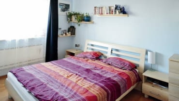 Sypialnia jakich wiele. Centralnie ustawione łóżko z szafkami nocnymi po bokach, a na ścianach pomalowanych na chłodny błękit - półeczki na książki i drobiazgi. Jest tu wszystko, co potrzebne do wypoczynku. Prócz nastrojowej atmosfery.