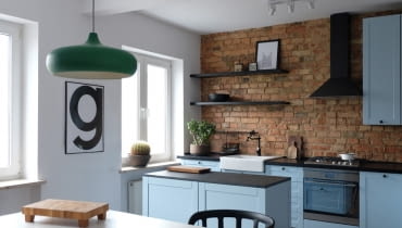 Pastelowy kolor szafek kuchennych pięknie koresponduje z surową cegłą. W kuchni pełno sentymentalnych nawiązań, jak stylizowany kran czy uchwyty szafek. Czarne dodatki harmonizują tonację. wnętrza retro, vintage, aranżacja wnętrz