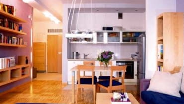 Aneks kuchenny jest integralną częścią salonu. Jasne, gładkie fronty szafek i przeszklone witrynki dają wrażenie lekkości, nie przytłaczają więc wnętrza.