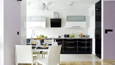 Fronty dolnych szafek kuchennych oraz drzwi wysokiej szafy-spiżarki są z czarnego szkła ujętego w aluminiowe ramki. Górne szafki, częściowo przeszklone, zrobiono z płyty MDF lakierowanej na wysoki połysk. Ze względów praktycznych podłogę przy ciągu roboczym wyłożono płytami gresu. Stół ustawiony na granicy kuchni i pokoju dziennego jest niewielki, ale po rozłożeniu może przy nim zasiąść aż osiem osób.