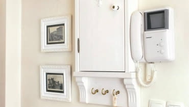 Dzięki naszemu pomysłowi przedpokój z zainstalowanymi na ścianie licznikami lub bezpiecznikami będzie wyglądał bardzo stylowo. Pokazana szafka jest łatwa do zrobienia i - co ważne - niedroga. <BR />Skrzynkę z licznikami lub bezpiecznikami najprościej jest ukryć w szafie ubraniowej - będą tam niewidoczne, a zarazem dostępne w razie potrzeby. Często jednak umiejscowienie tych niezbędnych, lecz nieatrakcyjnych urządzeń jest tak niefortunne, że nie ma mowy o jakiejkolwiek funkcjonalnej skrytce. Tak było w tym przypadku, stąd decyzja o zrobieniu ozdobnej miniszafeczki zharmonizowanej z wystrojem całego przedpokoju. Świetnym rozwiązaniem było umieszczenie obok szafki małych czarno-białych fotografii oprawionych w białe ramki - stanowią przeciwwagę wiszącego po prawej stronie domofonu.