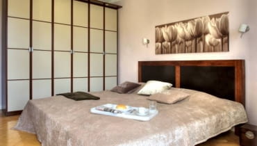 Sypialnia. Podwójne łóżko z egzotycznego drewna ma wysoki zagłówek wyłożony ciemną skórą. Boczną ścianę sypialni zabudowano szafą z przesuwanymi drzwiami w japońskim stylu. WNETRZA , POKOJ , SYPIALNIA , MEBLE - SZAFA WNEKOWA , LOZKO