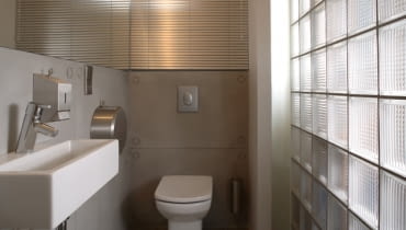 Pomysłowe rozwiązania mogą uczynić nawet z najmniejszej łazienki atrakcyjną toaletę gościnną. Szybkie spojrzenie na wnętrze wiele mówi o stylu właścicieli. Na zdjęciu mała łazienka optycznie powiększona przez przezroczystą ścianę - tutaj z luksferów (szklanych pustaków). łazienka dla gości, łązienka gościnna, łazienka zdjęcia, toaleta gościnna