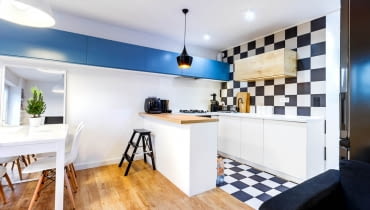 Elementem spajającym kuchnię z pozostałą częścią pomieszczenia jest ciąg szafek biegnących wysoko wzdłuż ściany.