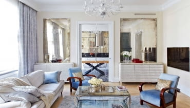 Pod symetrycznymi taflami postarzanych luster (Renes) stoją komody projektu Marii Kowalewskiej pokryte płatkami srebra. Jedna pełni funkcję barku, druga kryje sprzęt audio wideo. Kanapy (MTI Furninova), szklany stolik Cruise (BBHome). W głębi widoczna kuchnia i jadalnia.