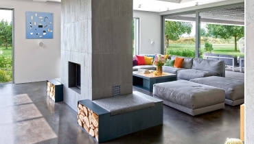 Wypoczynkowy obszar strefy dziennej wytycza dwustronny kominek - geometryczna forma z delikatnie ryflowanego betonu. Szarą paletę wnętrza dopełnia obraz Marii Widelak. Wypoczynkowy obszar strefy dziennej wytycza dwustronny kominek - geometryczna forma z delikatnie ryflowanego betonu. Szarą paletę wnętrza dopełnia obraz Marii Widelak.