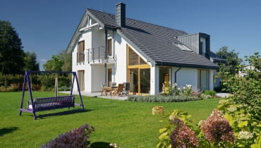 Dom wybudowany według projektu Doskonały ma klasyczny dwuspadowy dach, ale asymetryczny - co sprawia, że nabiera nowoczesnego charakteru dom nowoczesny, huśtawka, duże przeszklenia, komin, lukarna