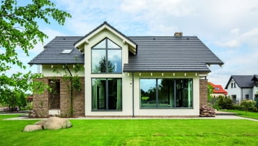 Tradycyjna forma o współczesnym wyglądzie sprawia, że dom łatwo jest wpasować nie tylko w zadbaną okolicę z elegancką stonowaną architekturą. Tego rodzaju zabudowa - nieepatująca ani nadmierną nowoczesnością, ani drastyczną stylizacją - może doskonale uspokoić i uporządkować również bardzo zabałaganione otoczenie ogród