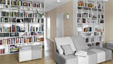 Dwa duże regały, zrobione na wymiar z malowanej płyty MDF, mieszczą domową biblioteczkę. Dwukolorowe, biało-szare meble wypoczynkowe (z firmy Agata) zdradzają zamiłowanie gospodarzy do spokojnych barw. salon, aranżacja salonu