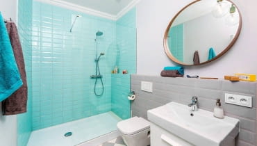 Błękitne płytki typu metro wyznaczają prysznic. W pozostałej części łazienki położono szare płytki. płytki ceramiczne, kolorowe płytki do łazienki