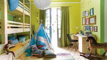 PO ZMIANIE. Do pokoju zamiast trzech oddzielnych łóżek, wprowadzono jedno trzypoziomowe. Dzięki temu na środku pokoju pozostało dużo wolnego miejsce do zabawy. Można na przykład ustawić namiot albo pobujać się na pięknym koniku na biegunach. Przez drzwi balkonowe wpada dużo światła. Zdobiące je zasłony są o kilka tonów ciemniejsze niż ściany. Roma Gąsiorowska, pokój dziecięcy