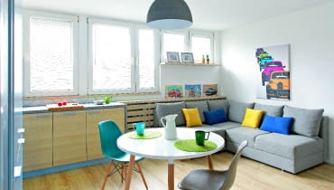 Po połączeniu kuchni z pokojem powstała spora strefa dzienna. Z jej nowoczesnym wystrojem harmonizują dekoracyjne dodatki nawiązujące do lat 60., kiedy wybudowano mieszkanie. Nadrukowane na blachach i na płótnie plakaty reklamujące osiągnięcia PRL-owskiej motoryzacji zostały kupione w sklepie Reset, który specjalizuje się w stylu vintage.