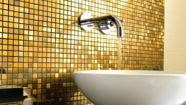 Łazienkę, zwłaszcza w miejscach narażonych na zachlapanie, najczęściej wykańczamy praktycznymi, trwałymi płytkami ceramicznymi - idealnymi do pomieszczeń, w których panuje wilgoć. Można je jednak zastąpić innymi materiałami. Jakimi? Mamy kilka sugestii. <BR /> ŁAZIENKA. Tapeta i szkło. Iście po królewsku: mieniąca się w świetle szklana mozaika w kolo-rze złota doskonale pasuje do dekoracyjnej ramy lustra.