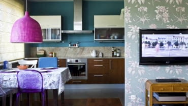 KOLOROWA I WESOŁA. Fantazyjne abażury: z pomalowanej na różowo wikliny oraz z koronki zastąpiły wiszące tu wcześniej lampy o prostych formach. Z kolorystyką wnętrza harmonizuje tapeta w kwiatowy wzór, którą pokryto ścianę przesłaniającą aneks kuchenny.