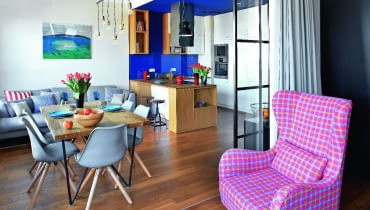 Jedną ze ścian w pokoju dziennym wyłożono... białymi płytkami gresu, których faktura przypomina malowane drewno. Na ich tle pięknie prezentuje się obraz Darii Samołyk "Jezioro z przebłyskiem". Fotel Greta i sofa Tokio pochodzą z firmy Sits, krzesła Lars Colour kupiono w Le Pukka. Kąt wypoczynkowy oświetla lampa Pole Six (z Kare Design) składająca się z sześciu żarówek zawieszonych na różnej wysokości. JEDNĄ ZE ŚCIAN w pokoju dziennym wyłożono... białymi płytkami gresu, których faktura przypomina malowane drewno. Na ich tle pięknie prezentuje się obraz Darii Samołyk "Jezioro z przebłyskiem". Fotel Greta i sofa Tokio pochodzą z firmy Sits, krzesła Lars Colour kupiono w Le Pukka. Kąt wypoczynkowy oświetla lampa Pole Six (z Kare Design) składająca się z sześciu żarówek zawieszonych na różnej wysokości.