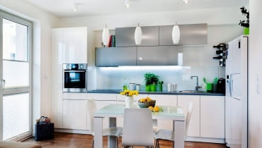 PRZECHOWYWANIE W KUCHNI. System trójkowy. Stół, stanowiący umowną granicę między strefami o różnej funkcji, oświetlają trzy lampy z podłużnymi kloszami, natomiast część kuchenną - oprawy sufitowe Massive Pillar. Pod górnymi szafkami dodatkowo zamontowano halogeny, których światło pada bezpośrednio na blat roboczy.