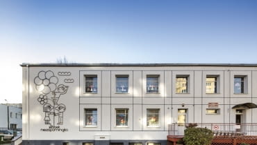 Odnowiony żłobek w Gdyni. Oszczędna w formie fasada, a na niej ilustracja metaloplastyczna zdradzająca funkcje budynku. Odnowiony żłobek w Gdyni. Oszczędna w formie fasada, a na niej ilustracja metaloplastyczna zdradzająca funkcje budynku
