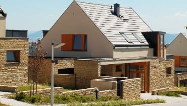 Osiedle domów jednorodzinnych - kamień na parterze, tynk na piętrze i powtarzające się drewniane elementy stolarki okiennej i drzwiowej Osiedle domów jednorodzinnych - kamień na parterze, tynk na piętrze i powtarzające się drewniane elementy stolarki okiennej i drzwiowej