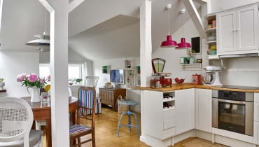 Słupy wyznaczają granicę między aneksem kuchennym a pokojem dziennym. Projektując kuchnię, pani domu zrobiła najpierw spis niezbędnych naczyń i akcesoriów, a następnie policzyła, ile potrzeba szuflad, by je wszystkie pomieścić. Gotowe sosnowe szafki z IKEA pomalowała na biało.