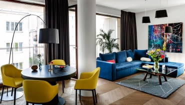 Dębowy parkiet ułożony w paryską jodełkę (komosinski.eu) nadaje wnętrzu modny, ale i ponadczasowy charakter. Obraz "Abstrakcja 5" Łukasza Stokowskiego (Galeria Ornament). Stolik ze szklanym blatem (Fritz Hansen), dywan (Hay Dot), filcowe lampy sufitowe Felt Shade Toma Dixona.