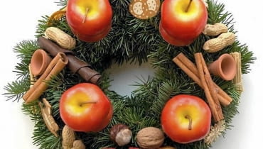 Ozdoby adwentowe. Wieniec ze świecami-jabłkami, laskami cynamonu, orzechami i drobnymi dekoracjami ceramicznymi