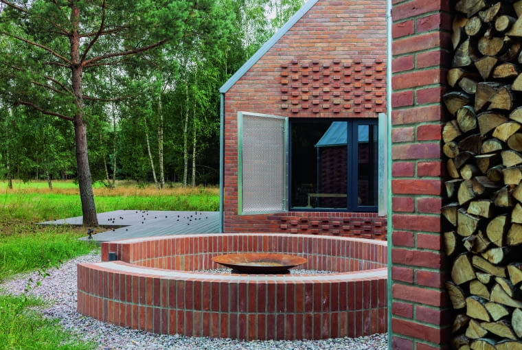 Między dwiema bryłami powstał miniplacyk, na którym architekt stworzył palenisko w kształcie okręgu – rozciąga się z niego widok na polanę, las i rzekę Pogorzeliczankę