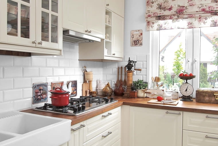 Kuchenną zabudowę ożywiają blaty z płyty imitującej orzechowe drewno (wszystko z IKEA). Kwiecista roleta rzymska (dekoria.pl) dodaje wnętrzu sielskiego klimatu.