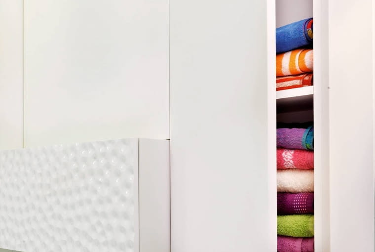 ŁAZIENKA. Fronty niektórych szafek wykonano z dekoracyjnych paneli (z płyty MDF). Oryginalna faktura zdecydowanie urozmaiciła jednolitą białą powierzchnię pozostałych szafek.