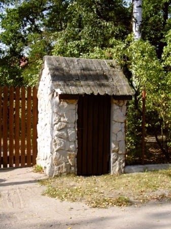 Śmietnik o rustykalnym wyglądzie: ściany z łamanego kamienia, dach kryty drewnem.