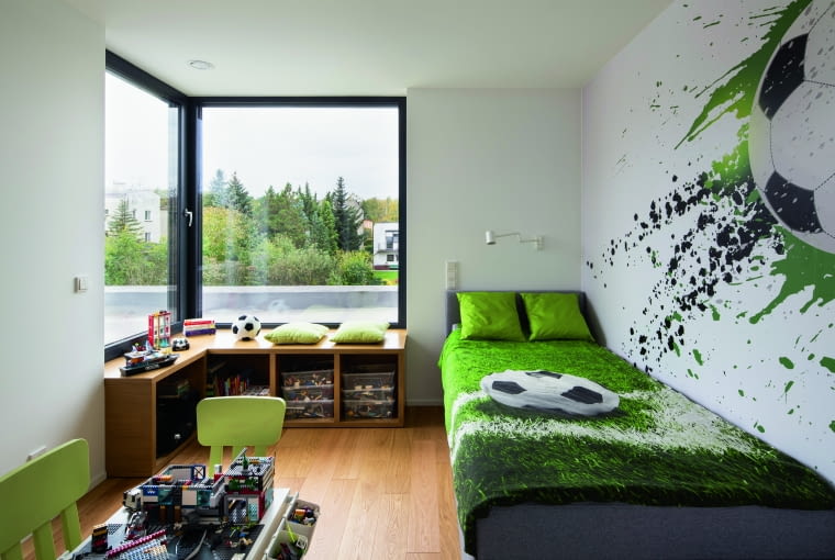 Pokój syna usytuowano na piętrze. Otwierają się tu widoki na ogród i sąsiedztwo działki, a także na futbolowe zainteresowania głównego lokatora. Minimalizm obowiązujący na parterze ulega lekkiemu zawieszeniu – jak to w dziecięcym królestwie Dom z kostki