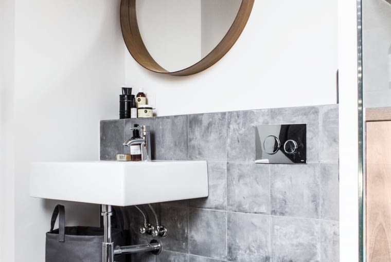 Tu także nie ma nudy. Graficzne wzory na posadzce, tekstylna torba zamiast tradycyjnego kosza na pranie i goła żarówka zamiast kinkietu. Bez zbędnego przepychu, a jednak elegancko.