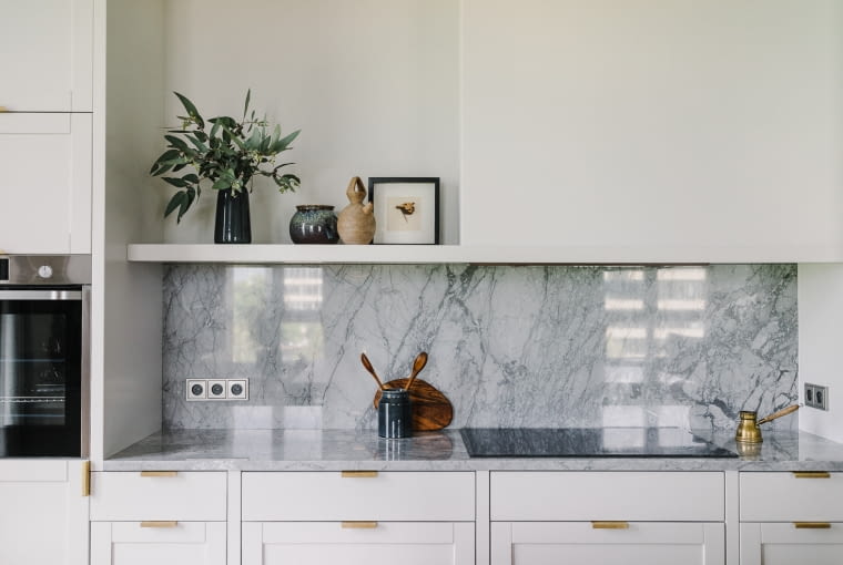 Kuchnia jest prosta i minimalistyczna. Marmur Bardiglio, którym pokryty jest blat i zabezpieczona ściana, stanowi odniesienie do szarości kominka w salonie, zabudowanego w betonowej oprawie.