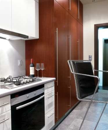 Szafy zabudowujące ścianę od góry do dołu są bardzo pojemne. Za drzwiczkami z długimi uchwytami kryją się nie tylko półki, ale także lodówka.