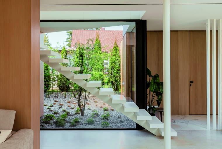 W strefie wejścia do domu widok na opisywany wcześniej miniogródek umieszczony we wcięciu w bryle przecinają zawieszone efektownie w powietrzu schody, łączące parter z górną kondygnacją. Przy pierwszych stopniach stoi jeden ze słupów stalowej konstrukcji budynku W strefie wejścia do domu widok na opisywany wcześniej miniogródek umieszczony we wcięciu w bryle przecinają zawieszone efektownie w powietrzu schody, łączące parter z górną kondygnacją. Przy pierwszych stopniach stoi jeden ze słupów stalowej konstrukcji budynku