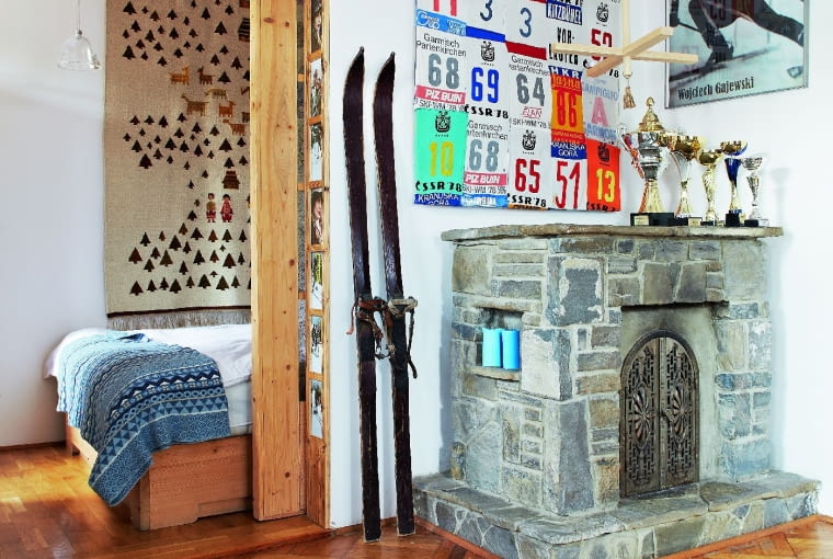 NA KOMINKU z rzecznego kamienia stoją trofea pana domu. Numery startowe tworzą na ścianie oryginalną kompozycję. We framudze drzwi prowadzących do sypialni znalazło się miejsce na rodzinne fotografie.