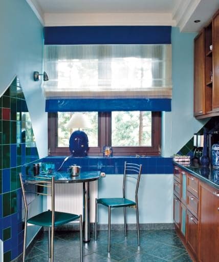 Styliści zachęcają do montowania rolet w oknach kuchennych. Uznają je za równie dekoracyjne jak zasłony i firany, a przy tym praktyczne i proste zarówno w montażu, jak i obsłudze. <BR />DEKORACJE - OKNO Z PRZEJRZYSTĄ ROLETĄ. Roleta rzymska została uszyta z przejrzystej tkaniny firankowej. Górę i dół wykończono pasami z podobnego materiału, ale w kolorze kobaltowym, takim jak większość płytek ceramicznych na ścianie. Obłożony drobnymi płytkami parapet pełni rolę półki. Można z niej swobodnie korzystać nawet po zaciągnięciu rolety.