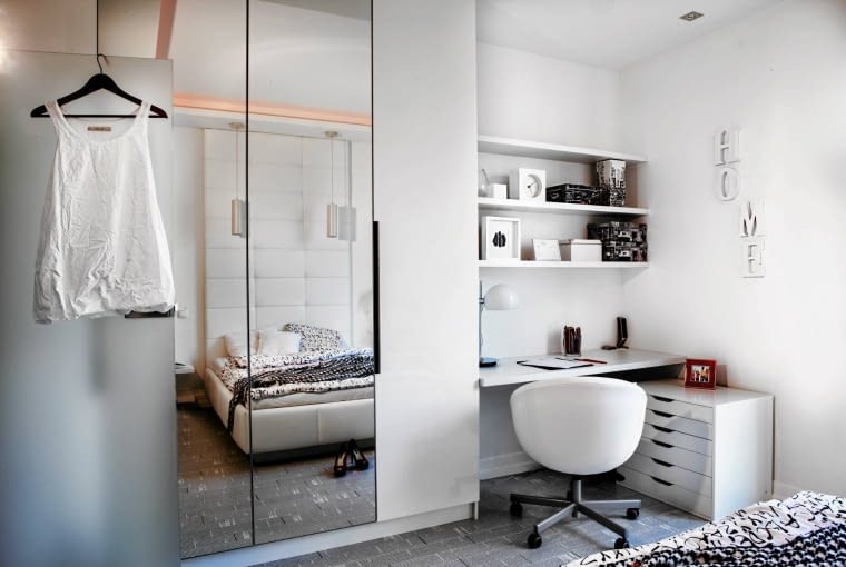 SYPIALNIA. Trzeba się dobrze przyjrzeć, by zauważyć, że szafa to w istocie dwa meble, ustawione tak, by sąsiadujące ze sobą fronty utworzyły duże lustro. Nie mają uchwytów - drzwi otwiera się, wsuwając palce do frezowanej szczeliny. W sporej wnęce między szafami a ścianą zaaranżowano miejsce do pracy. Nie trzeba było wstawiać tradycyjnego biurka - wystarczył blat i półki przycięte na wymiar u stolarza.