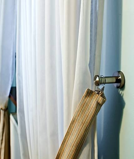 DEKORACJE - OKNO W ZWIEWNYM PRZYBRANIU. Każda firanka jest podpięta po obu bokach okna opaską uszytą z tej samej tkaniny, co lambrekin. Opaski zaczepia się do stalowych uchwytów przykręconych do ściany powyżej parapetu.