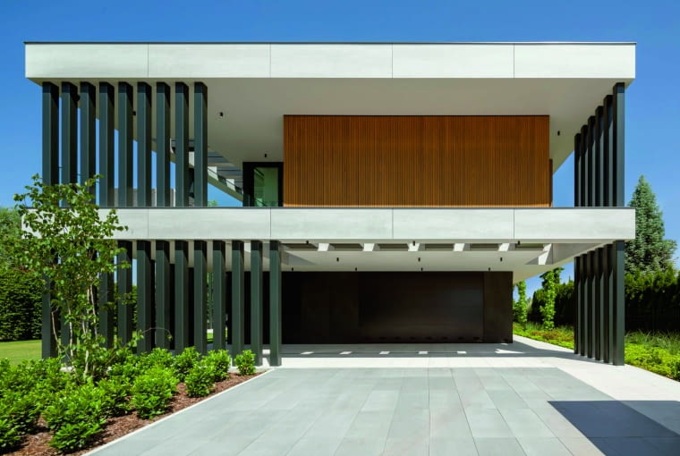 Każdy projekt domu z płaskim dachem świetnie wygląda   w ponadczasowej bieli połączonej z różnymi odcieniami szarości czy  brązów. A dodatkowe elementy, takie jak widoczne tu ażurowe słupy,  jeszcze mocniej podkreślają szlachetną elegancję i surowość bryły