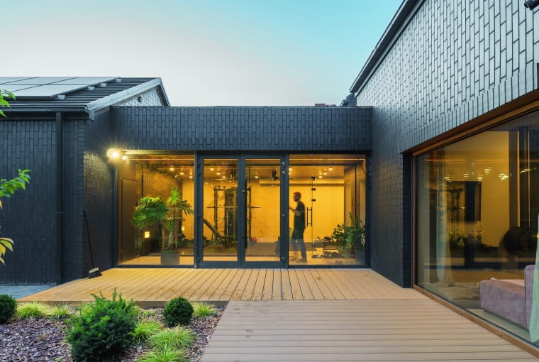 W module tym umieszczono obszerny wiatrołap, stanowiący jednocześnie trakt komunikacyjny między garażem i częścią mieszkalną, a za nim urządzono siłownię, czyli pomieszczenie sportowe. Dzięki obszernym przeszkleniom ćwiczący zachowują kontakt ze światem zewnętrznym W module tym umieszczono obszerny wiatrołap, stanowiący jednocześnie trakt komunikacyjny między garażem i częścią mieszkalną, a za nim urządzono siłownię, czyli pomieszczenie sportowe. Dzięki obszernym przeszkleniom ćwiczący zachowują kontakt ze światem zewnętrznym